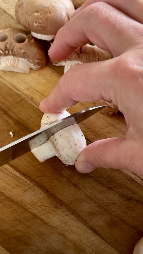 Slicing white button mushrooms vertically to make Halloween mushroom skulls