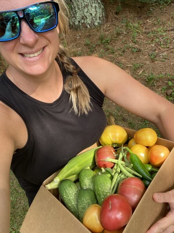 Chef Jen Galton holding a box of freshly picked produce- corn, cucumbers, tomatoes, green beans and jalapenos.