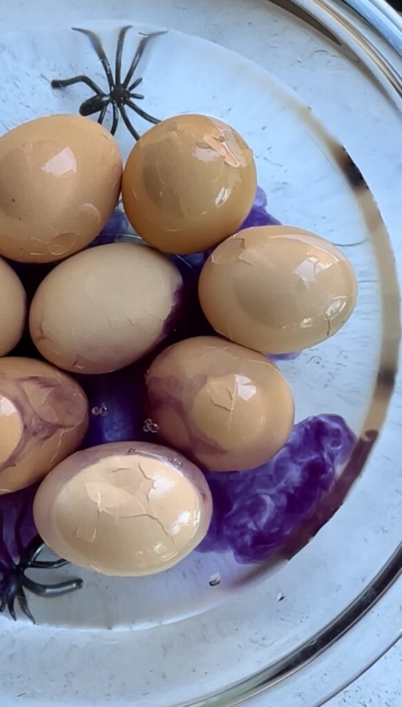 Adding vibrant purple food coloring to an overnight egg bath to dye spiderweb lines and create a creepy, veiny zombie eyeball design for a viral Halloween appetizer.
