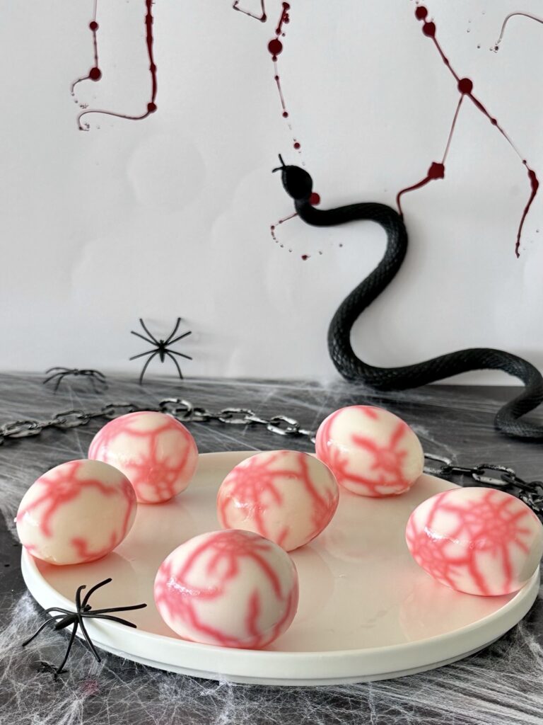 Naturally dyed Halloween eyeball deviled eggs with realistic bleeding red veins using plant-based food coloring.