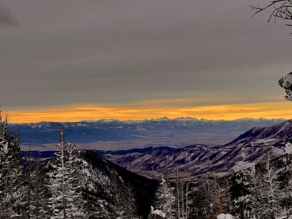 A breathtaking panoramic landscape view of a snow-covered mountain range in Bozeman Montana under a vibrant orange sunset sky.