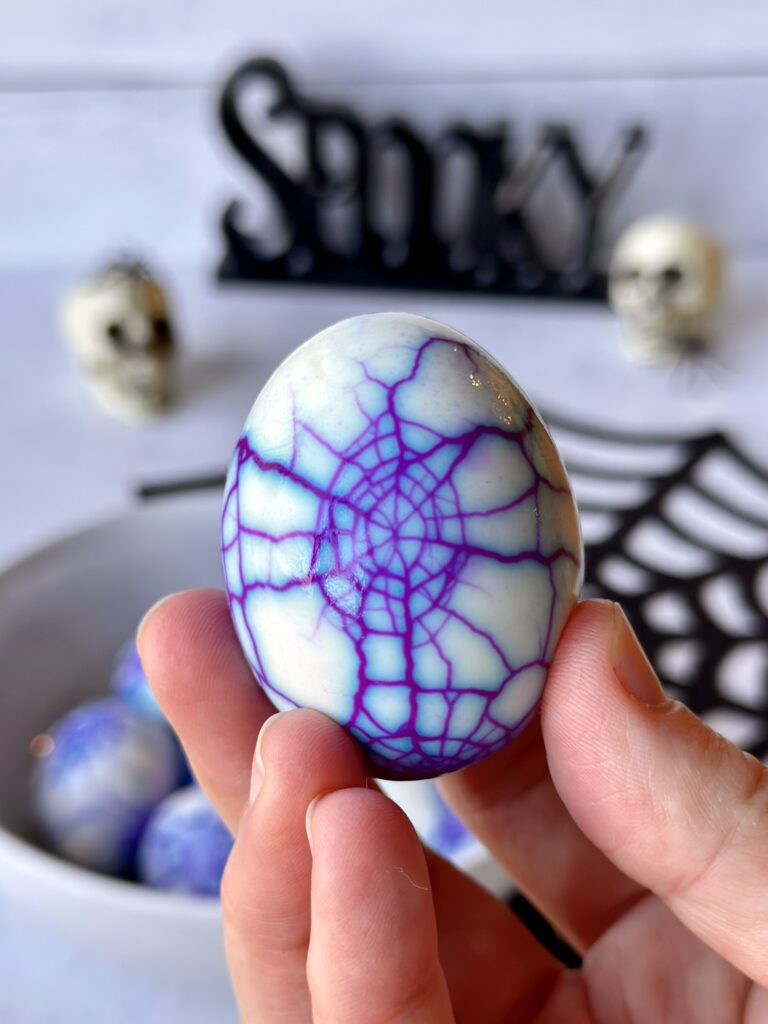 A hard-boiled egg showing a sharp, vibrant purple spiderweb pattern created with artificial US food dye for Halloween