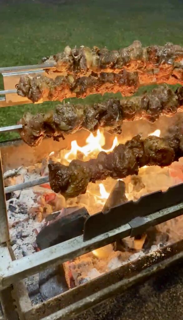 Greek style marinated lamb chunks on large metal skewers spinning over an open charcoal grill