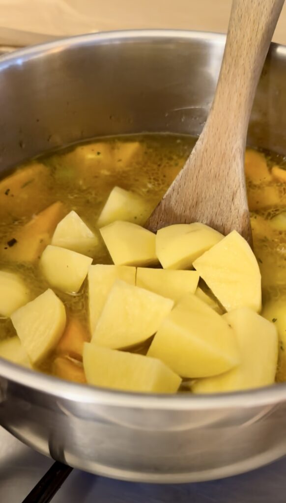 Add raw chopped potatoes into a simmering pot of butternut squash soup vegetables.
