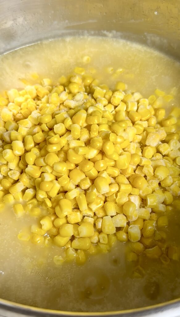Adding peeled potatoes and frozen corn to a simmering chowder broth