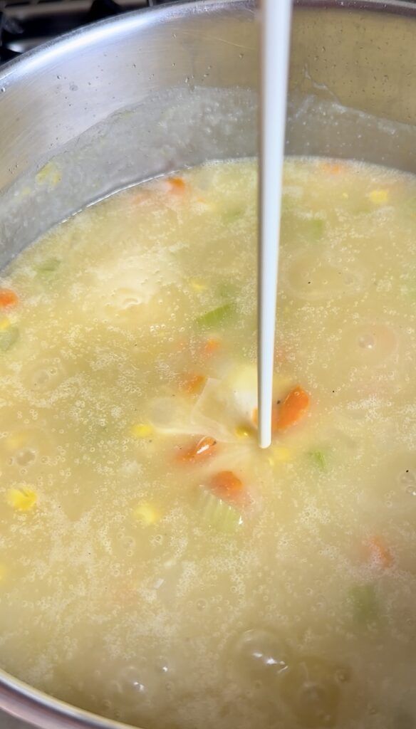 Pouring a stream of heavy cream into a thick, simmering corn chowder