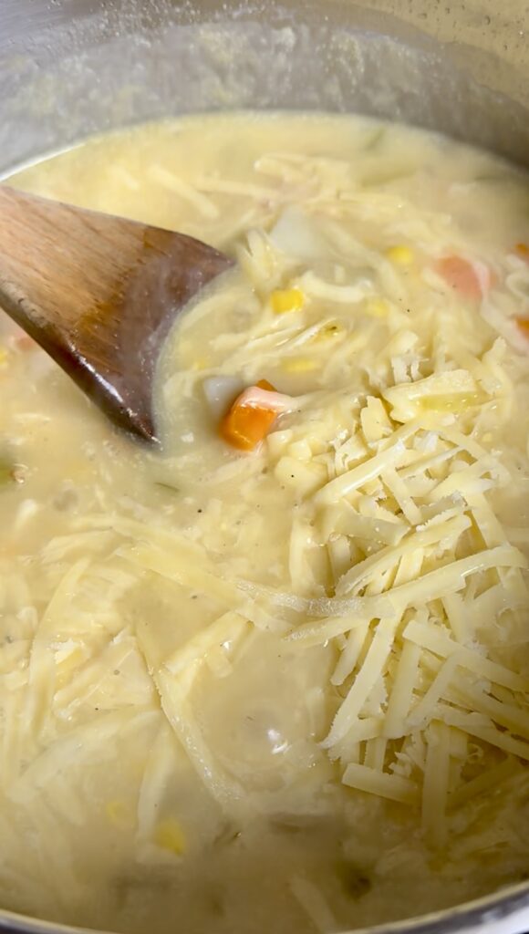 Stirring a layer of grated white cheddar and parmesan cheese into hot soup