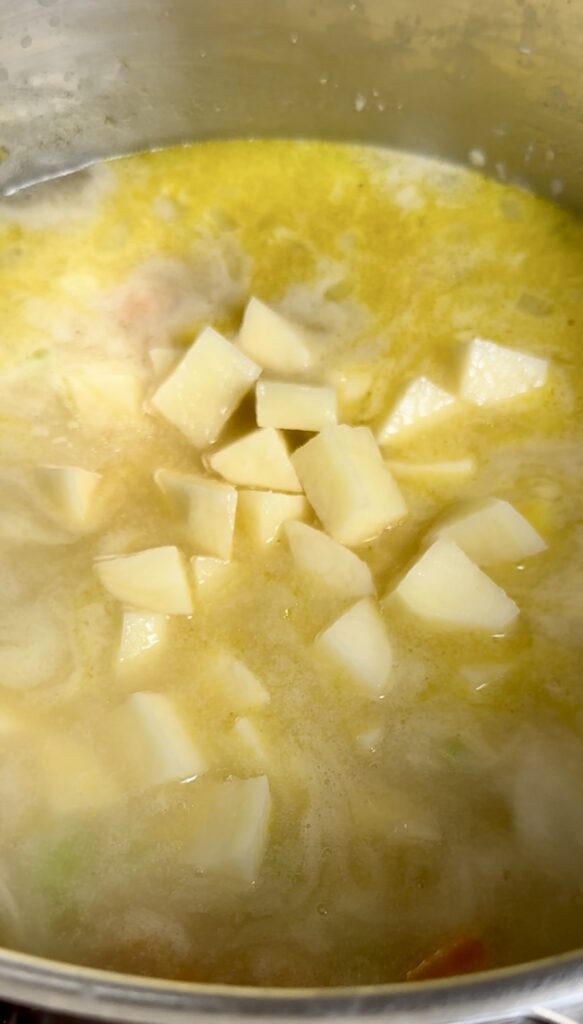 Adding peeled potatoes and frozen corn to a simmering chowder broth