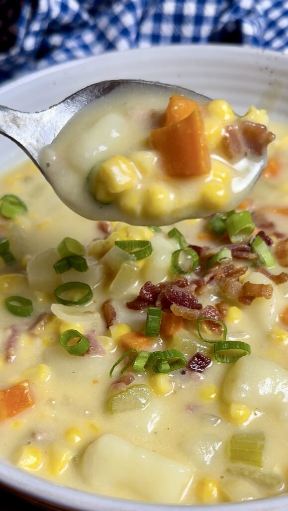 Close up spoon scoop of creamy bacon corn chowder garnished with green onions and crispy bacon bits