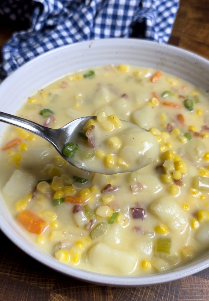 Close up spoon scoop of creamy bacon and corn chowder garnished with crispy bacon and green onions