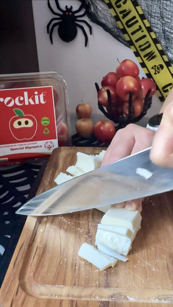 Prepping white chocolate blocks on a cutting board for Halloween candy apples. Chopping blocks of white baking chocolate with a large kitchen knife on a wooden cutting board