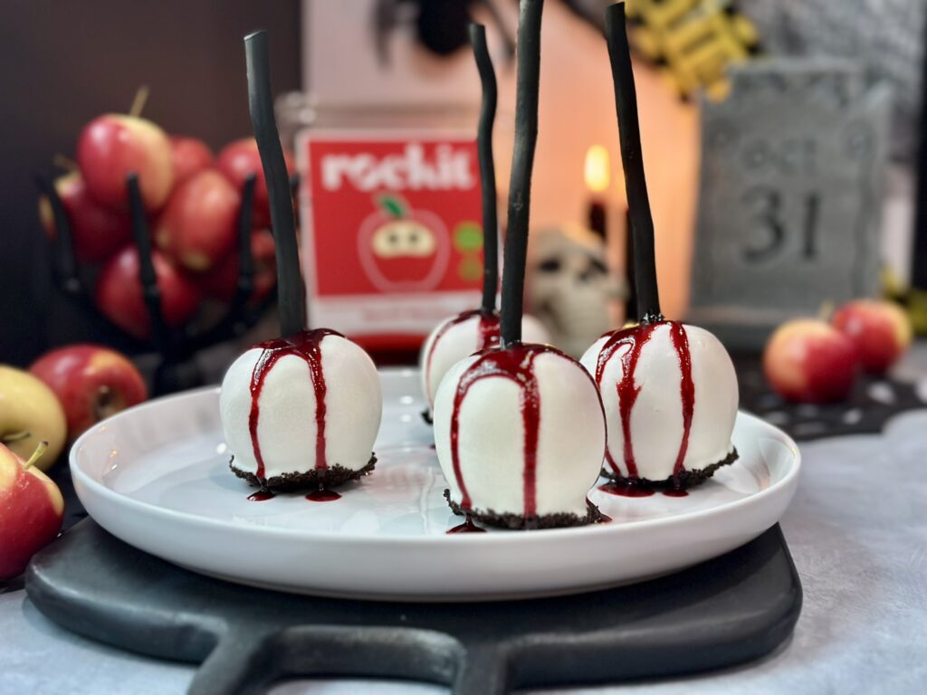 Gothic Bleeding White Chocolate Candy Apples Full Scene Setup Gothic white chocolate bleeding candy apples on a dark Halloween dessert table with candles, tombstone and skull props setting a spooky scene.