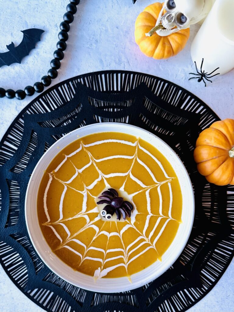 An overhead flat lay view of a completed festive Halloween butternut squash soup bowl surrounded by spooky decorations.