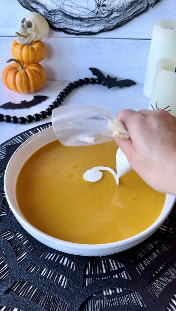 Piping a heavy cream circle in the center of an orange bowl of soup to start a spiderweb pattern.