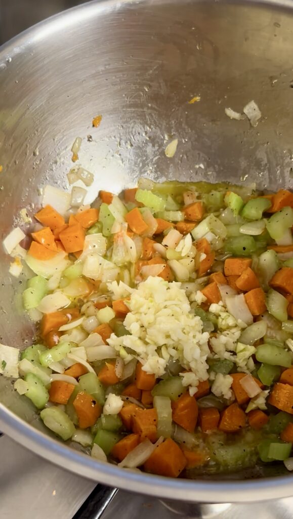 Chopped carrots, celery, onion cooking with minced garlic and fresh rosemary in a soup pot.